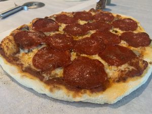 Picture of a cooked pizza that has red sauce, melted shredded cheese and pepperoni for toppings.