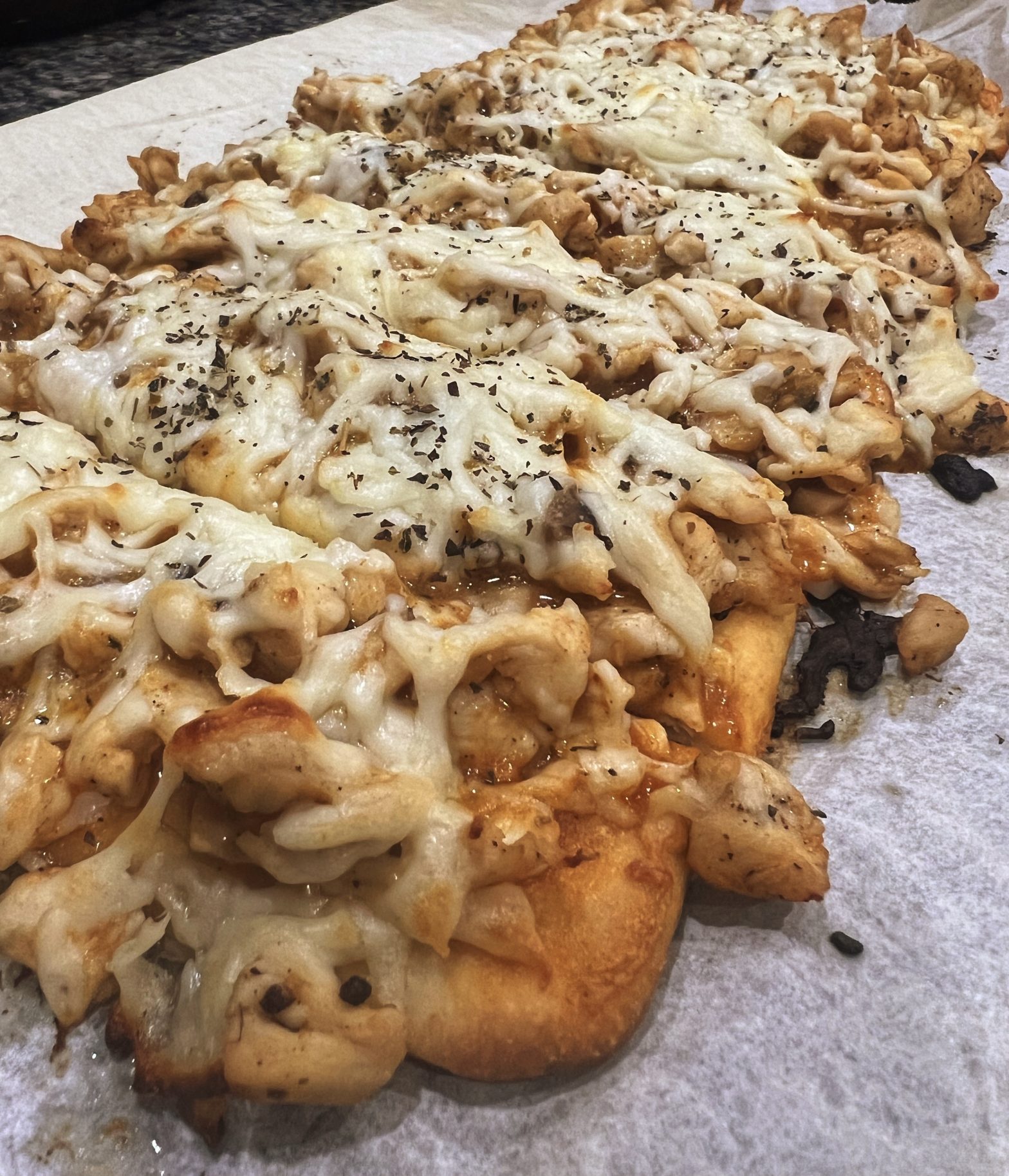 A picture of a piece of flat bread baked and topped with buffalo sauce, melted mozzarella (white cheese), diced chicken breast, mushrooms and onions.