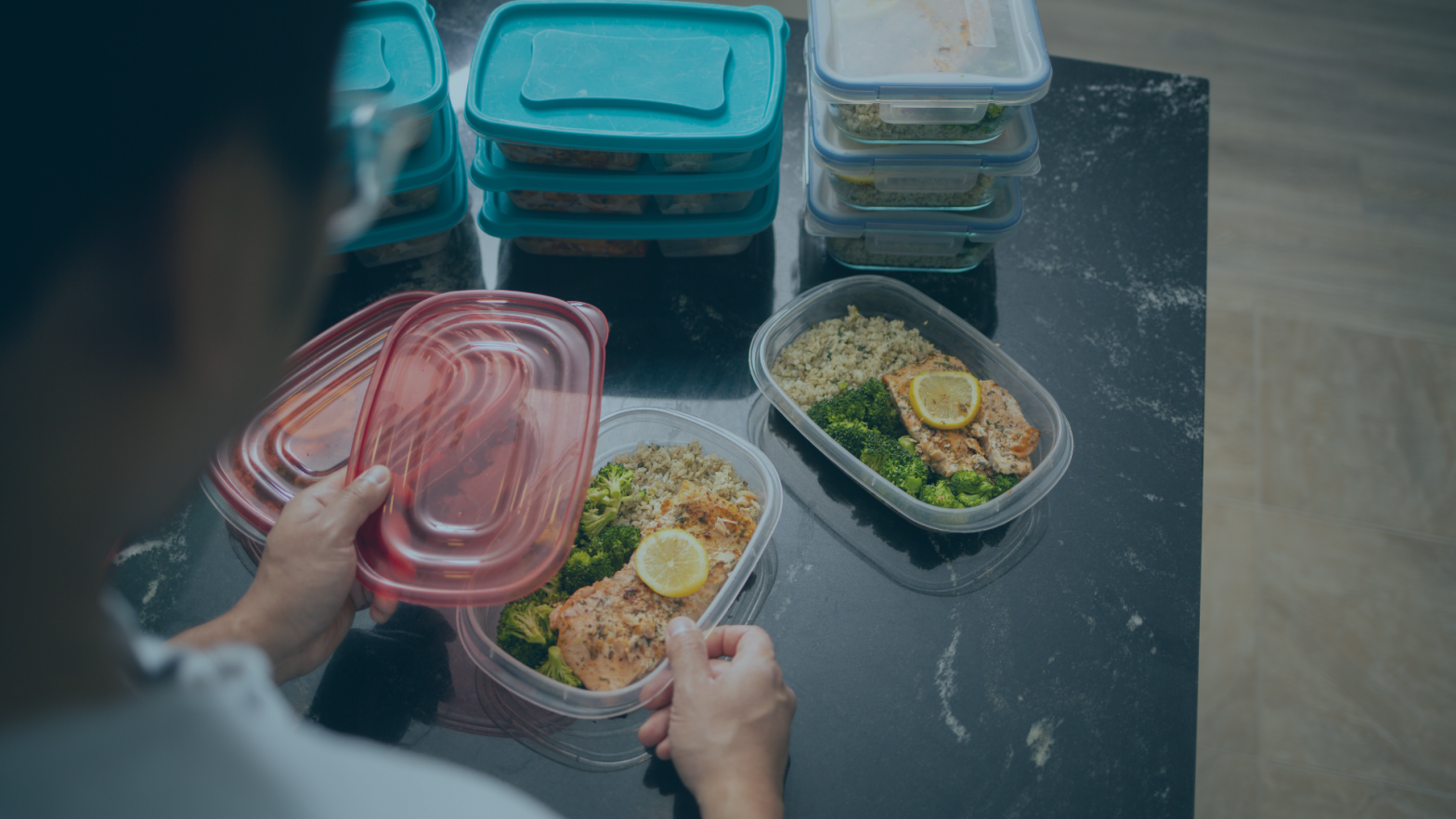 Person meal prepping with containers of rice, vegetables, and protein on a kitchen counter.