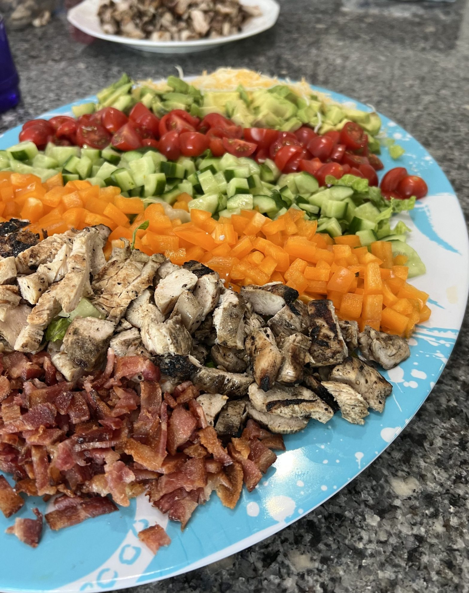 Grilled chicken cobb salad with lettuce, bacon, avocado, tomato, cucumber, and peppers — homemade and served on a white plate.
